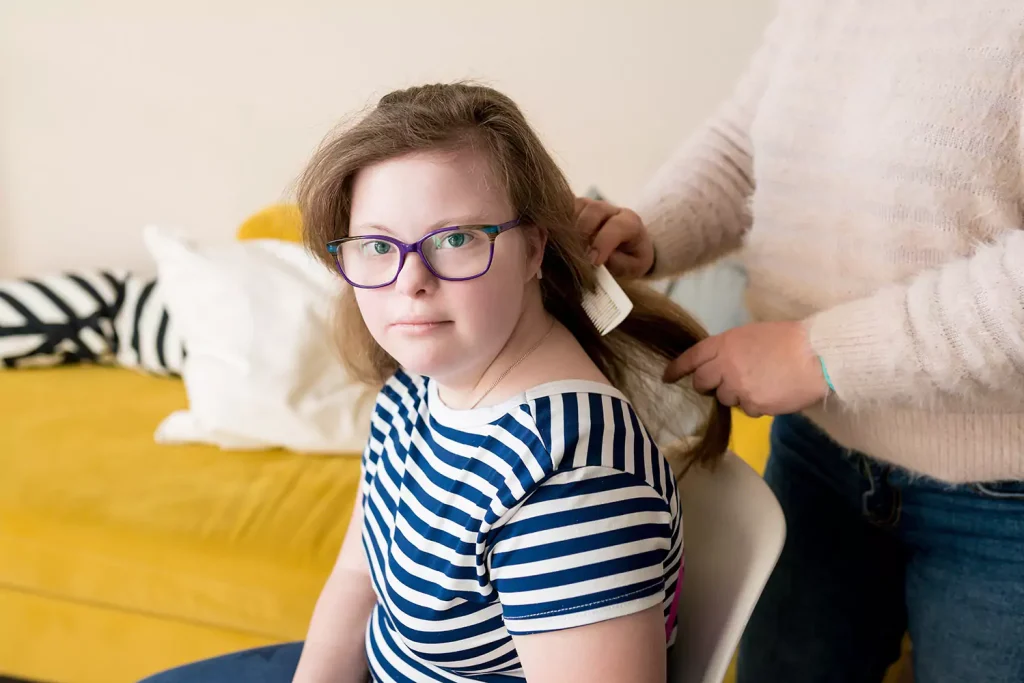 A young woman with down syndrome is getting her hair brushed by her care giver