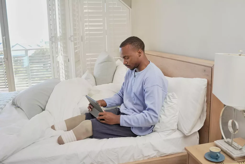 A physically disabled man is using his tablet device while sitting in bed