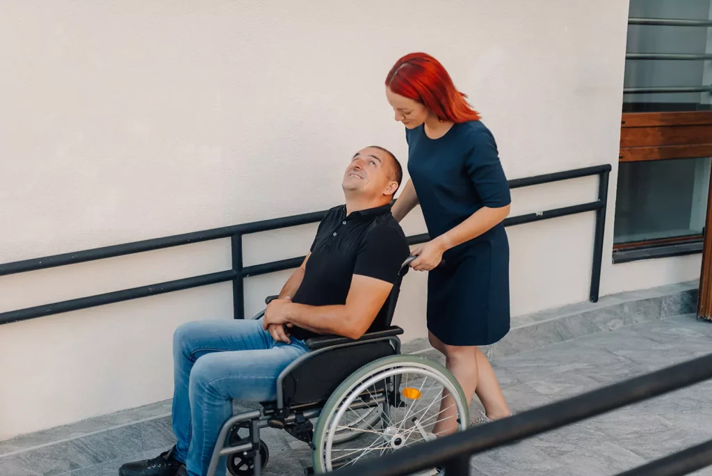 A care provider is pushing a disabled man in a wheelchair outdoors